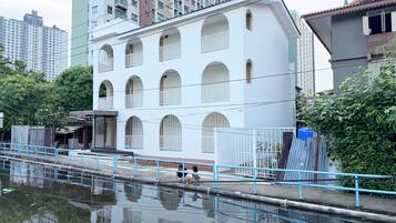 Un edificio de varios pisos con ventanas arqueadas y balcones, junto a una masa de agua con barandilla azul.