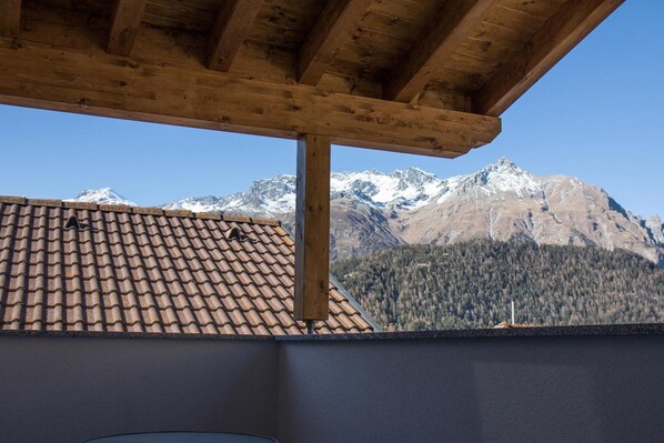 A wooden pergola structure with a view of snow-capped mountains and a forested valley.