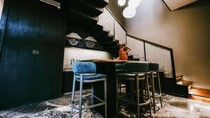 A modern kitchen with a marble floor, a bar area with stools, and a staircase with a geometric pattern. - Moonstone Luxury Villa (Badung)