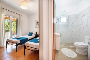 Une chambre d’hôtel avec un lit, une table de chevet, une fenêtre donnant sur un espace verdoyant, une salle de bain avec des toilettes, une douche et un mur en marbre.