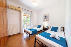 A hotel room with two beds, a radiator, a window with curtains, a painting on the wall, and a door with a handle. - Kallithea House Corfu - Courtyard & Beach Days (Gouvia)