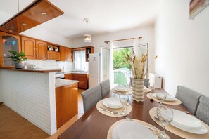 A modern kitchen with wooden cabinets, a built-in island, and a dining area with a table set for four. - Kallithea House Corfu - Courtyard & Beach Days (Gouvia)