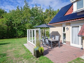 Eine Terrasse mit Tisch und Stühlen, einer Glaskonstruktion und einem Solarmodul auf dem Dach.