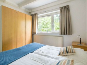 Ein Schlafzimmer mit einem Bett, einem Kleiderschrank, einem Fenster mit Vorhängen und einem Nachttisch mit Lampe.
