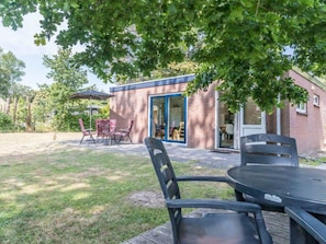 Eine Terrassenfläche mit Tisch und Stühlen, ein überdachter Sitzbereich und ein Gebäude mit einer blauen Tür.