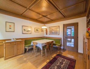 A dining area with a wooden ceiling, a green bench, a table with chairs, and a patterned rug. - Apartment in Aufhofen With Swimming Pool (Brunico)