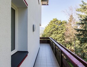 A narrow balcony with a tiled floor, a wooden railing, and a view of trees and mountains in the background. - Apartment in Aufhofen With Swimming Pool (Brunico)