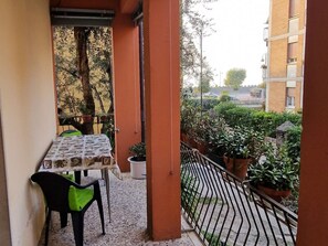 A balcony with a table and chairs, potted plants, and a view of a residential area. - Casa Rosario e Annamaria (Torri del Benaco)