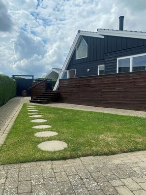 A modern house with a sloped roof, a wooden deck, and a paved pathway with circular stepping stones.