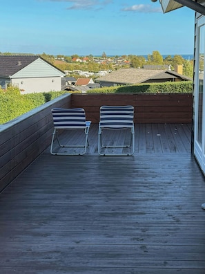 A wooden deck with two striped lounge chairs facing a view of a residential area and the sea. - Summer house with terrace towards Kerteminde Bay (Kerteminde)