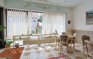 A room with a dining table and chairs, a radiator, a window with curtains, and a view of a building outside. - Group Accommodation Aquarium | 28 Persons | Sauna | in Monschau (Monschau)
