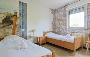 A bedroom with two beds, a stone wall, a window with blinds, and a beach-themed painting. - Group Accommodation Aquarium | 28 Persons | Sauna | in Monschau (Monschau)