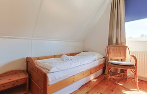 A single bed with a wooden frame and white bedding, a wooden nightstand, a wicker chair, and a window with a view. - Watersnip - Enjoying the water (Lemmer)