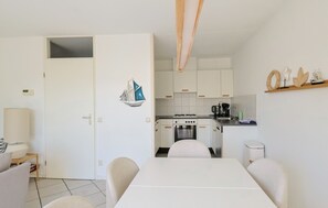 A compact kitchen with white cabinets, a stove, and a sink. There is a dining table with chairs in the foreground. - Watersnip - Enjoying the water (Lemmer)