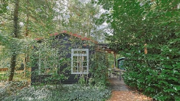A garden with a small wooden structure, surrounded by dense foliage and a pathway leading to a seating area.