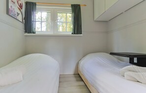 Una habitación con dos camas, una ventana con cortinas, una mesita de noche y un estante en la pared.