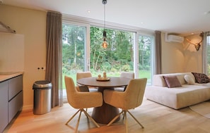 A modern living room with a round dining table, two chairs, a sofa, and a view of a lush garden through large windows. - De Tilgrup in Oude Willem (Oude Willem)