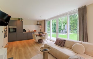 Un espacio habitable moderno con cocina, comedor y un amplio ventanal con vistas a un jardín.