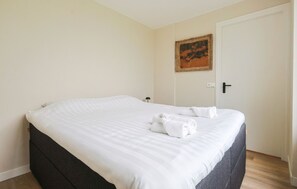 Una cama bien hecha con sábanas blancas y toallas dobladas, un cuadro en la pared y una puerta con pomo negro.