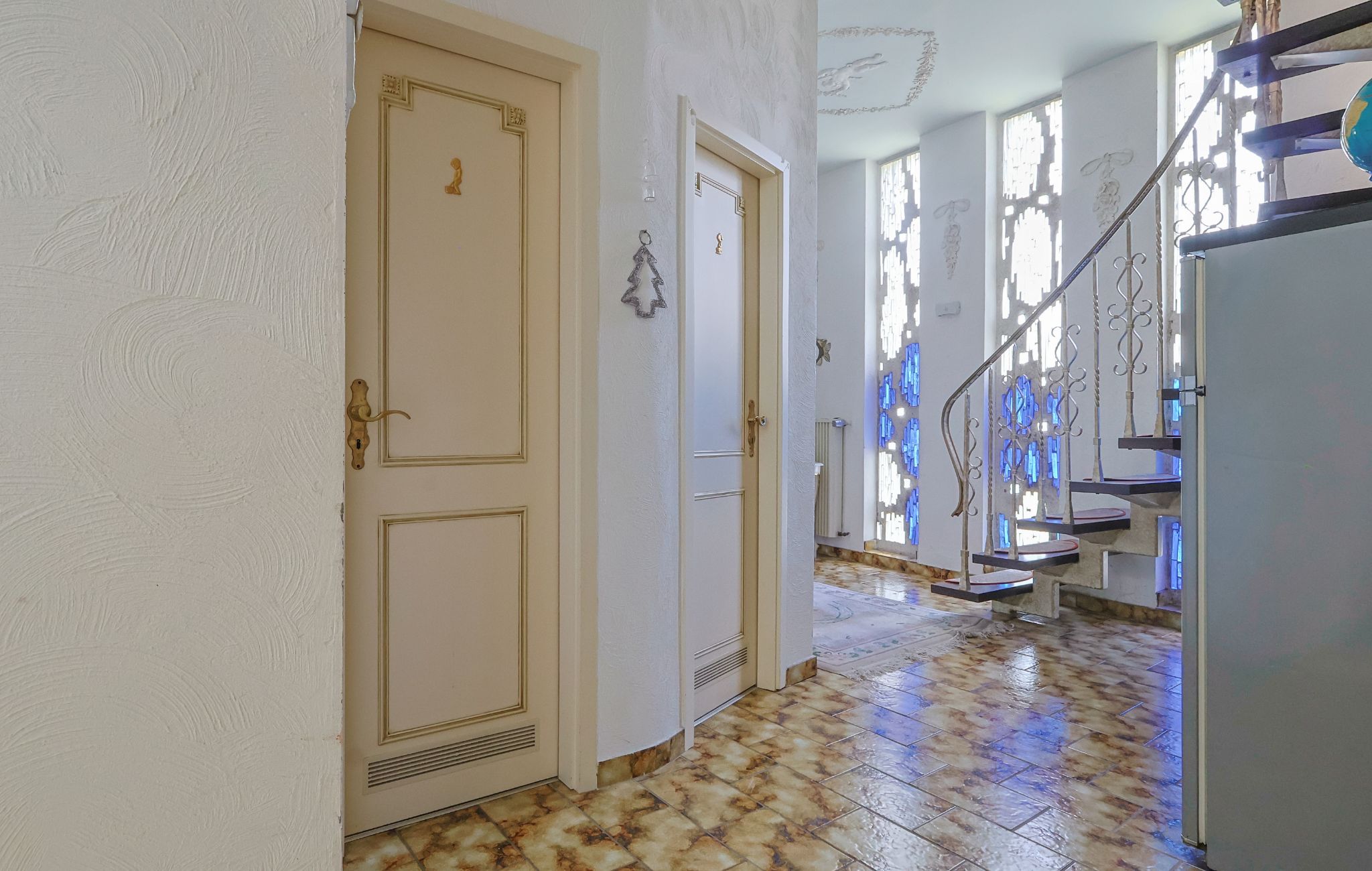 Un pasillo con piso de baldosas, una puerta con picaporte de latón y una escalera con barandilla de metal.