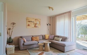 A living room with a grey sectional sofa, a wooden pegboard wall art, a floor lamp, and a view of the outdoors through a large window. - Waterfront Villa Strikel 18 Terherne (Terherne)