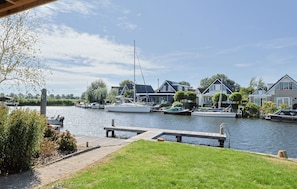 A riverside view with boats docked, a wooden dock, and houses with a grassy foreground. - Waterfront Villa Strikel 18 Terherne (Terherne)