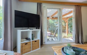 A living room with a television, a white entertainment unit, wicker baskets, and a sliding glass door leading to an outdoor patio. - Tiny house in the forest near Veluwezoom (Hattemerbroek)
