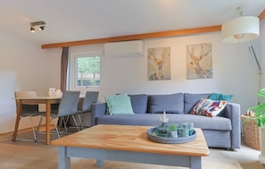 A modern living room with a grey sofa, a wooden coffee table, and a dining area with chairs and a table. - Tiny house in the forest near Veluwezoom (Hattemerbroek)