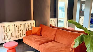 A modern lobby with a sectional sofa, two red stools, a large potted plant, and a decorative white railing.