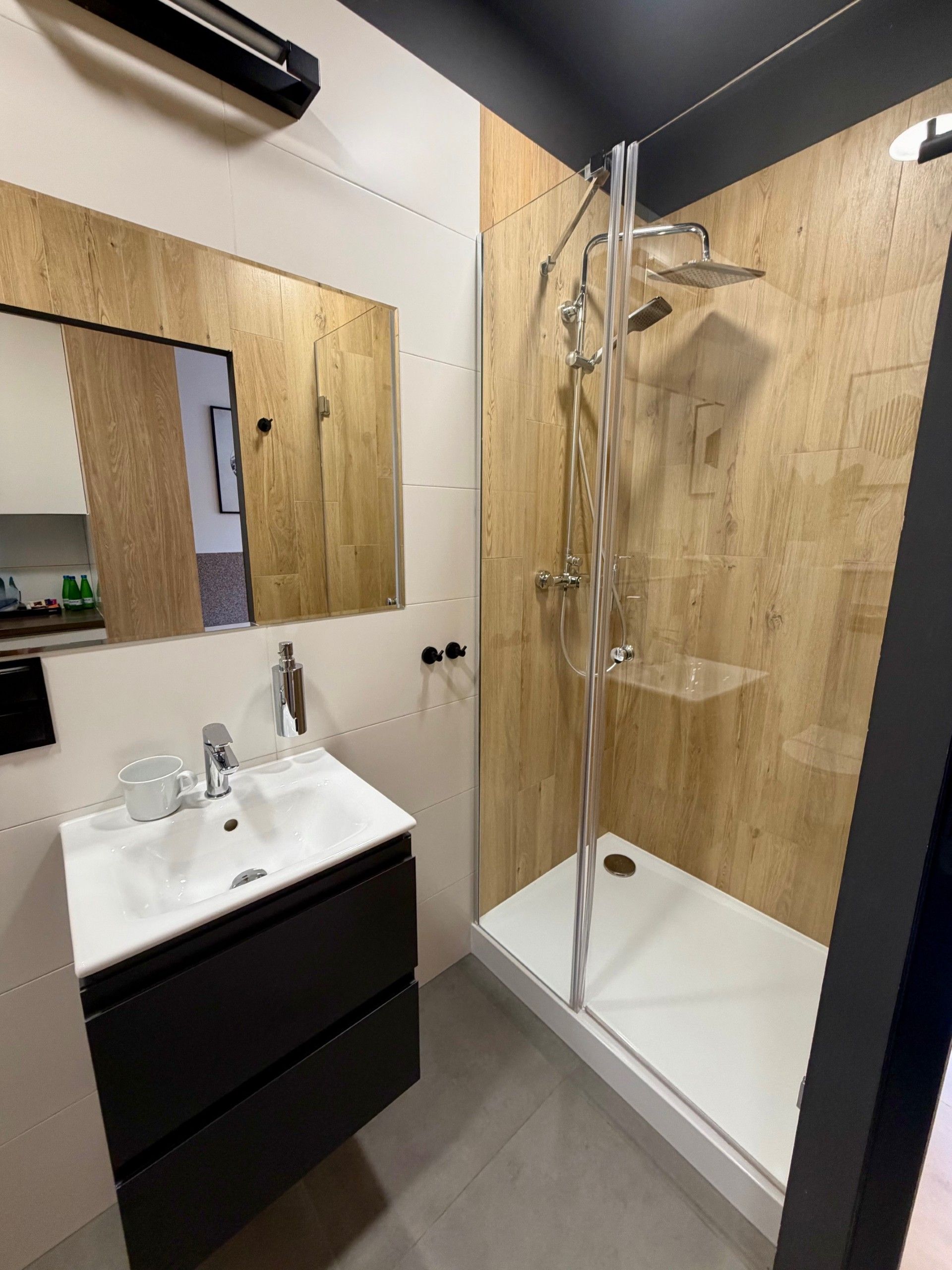 A modern bathroom with a glass-enclosed shower, a white sink, and a wooden vanity.