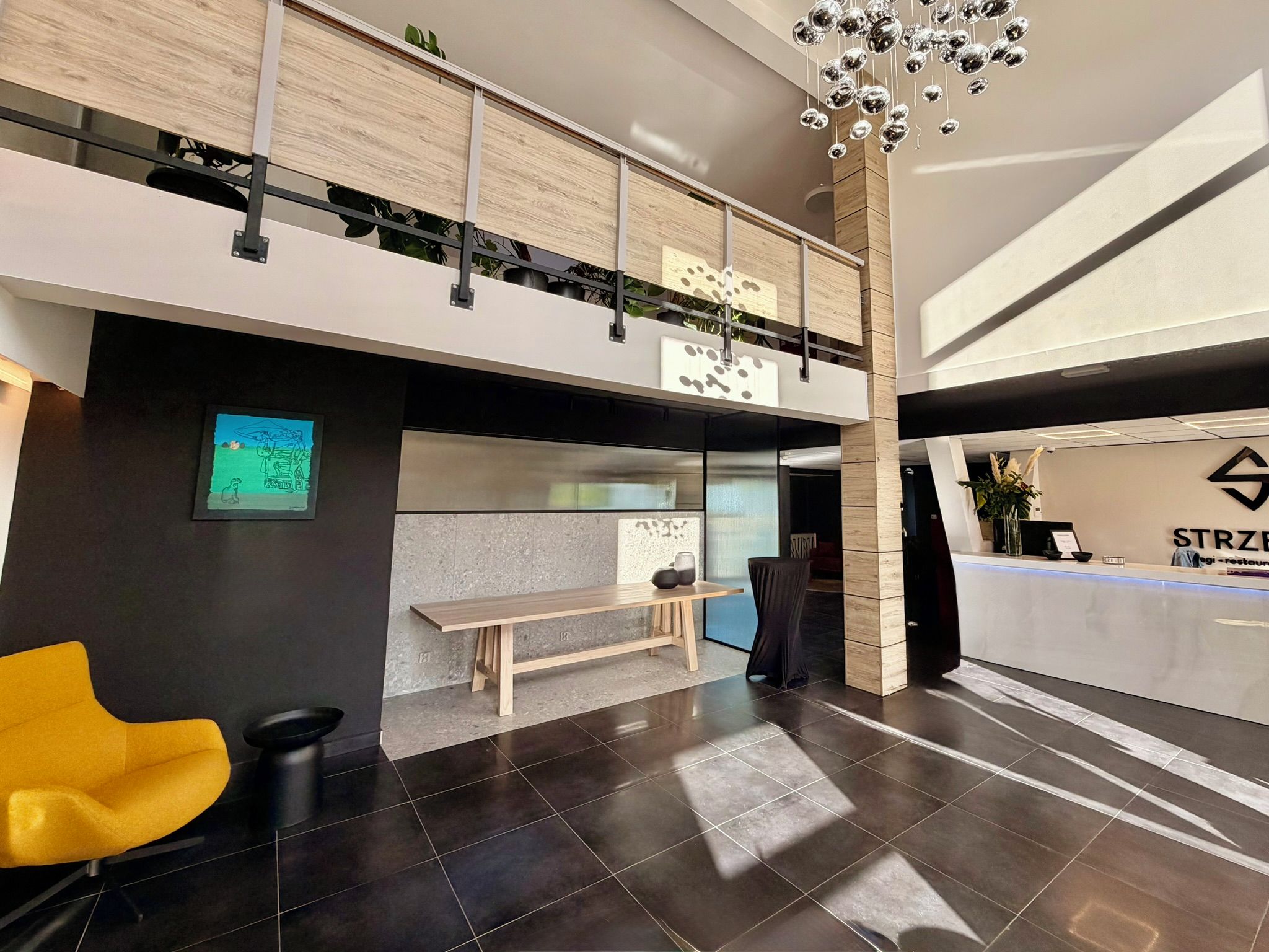 A modern hotel lobby with a reception desk, seating area, and a mezzanine level.