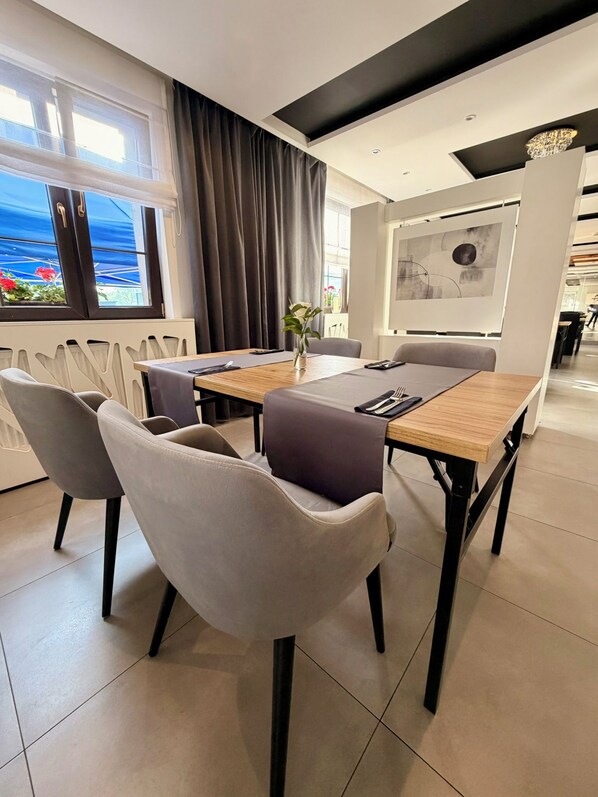 A modern dining area with a wooden table, grey upholstered chairs, and a view of the outdoors through large windows.
