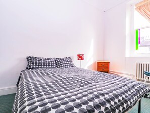 Ein Schlafzimmer mit einem Bett, einem Nachttisch, einer roten Lampe und einem Fenster mit Vorhängen.