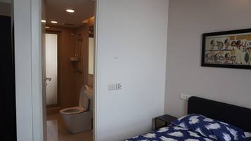 Ein Schlafzimmer mit einem Bett, einem kleinen Nachttisch, einem Wandbild und einem Badezimmer mit Toilette und Dusche.