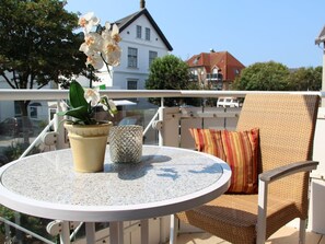 A round table with a potted orchid and a decorative candle, a wicker chair with a striped cushion, and a balcony railing. - 5 Boysenstr. 15 (Sylt)