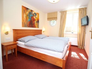 A hotel room with a wooden bed, a nightstand, a wall-mounted TV, and a large abstract painting. - 5 Boysenstr. 15 (Sylt)