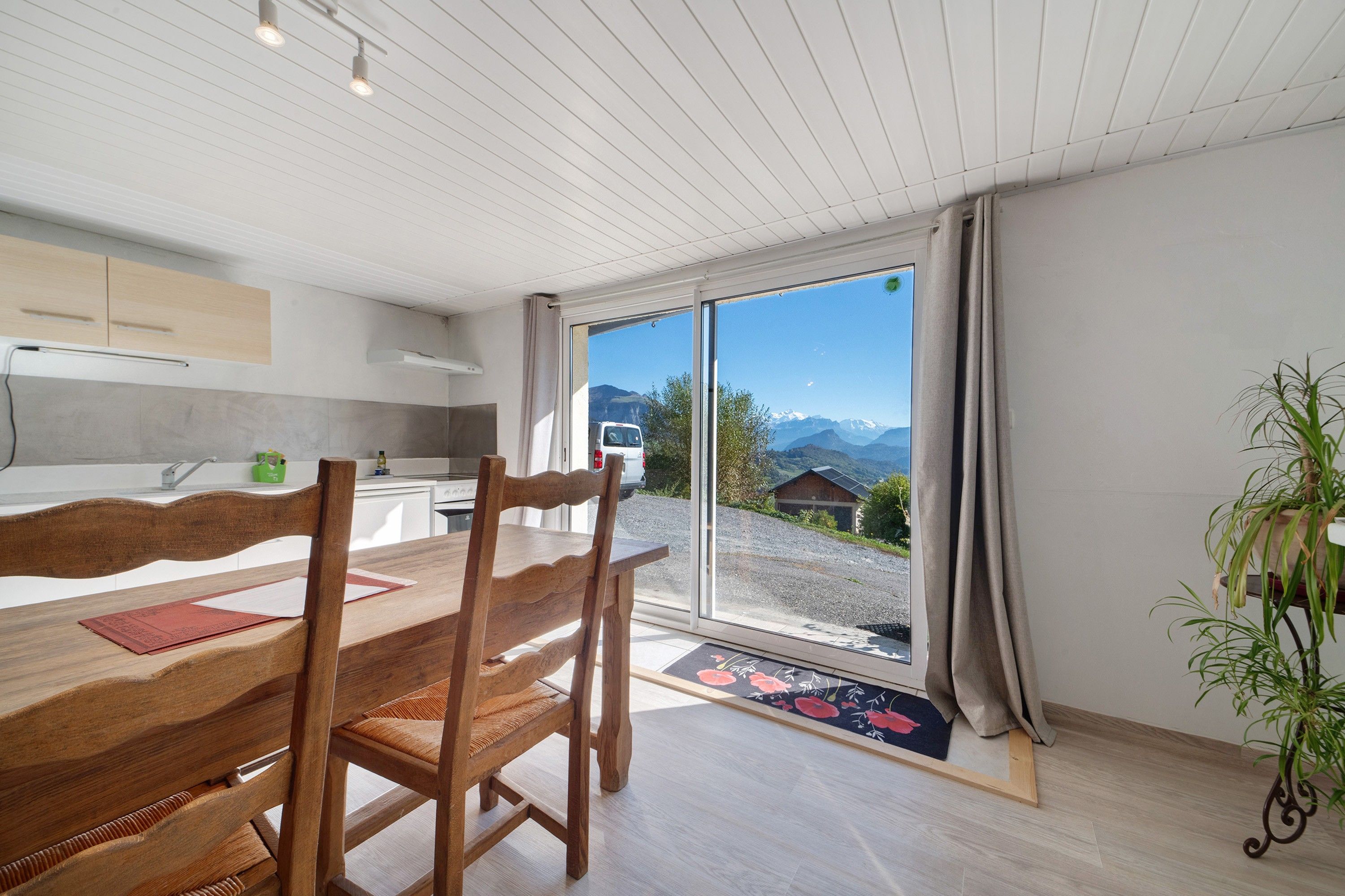 A modern kitchen with a dining area, a large sliding glass door leading to a scenic mountain view, and a potted plant.