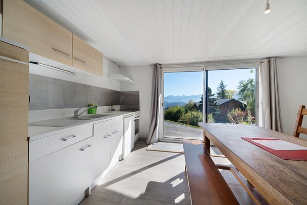A modern kitchen with a view of a mountainous landscape through a sliding glass door.