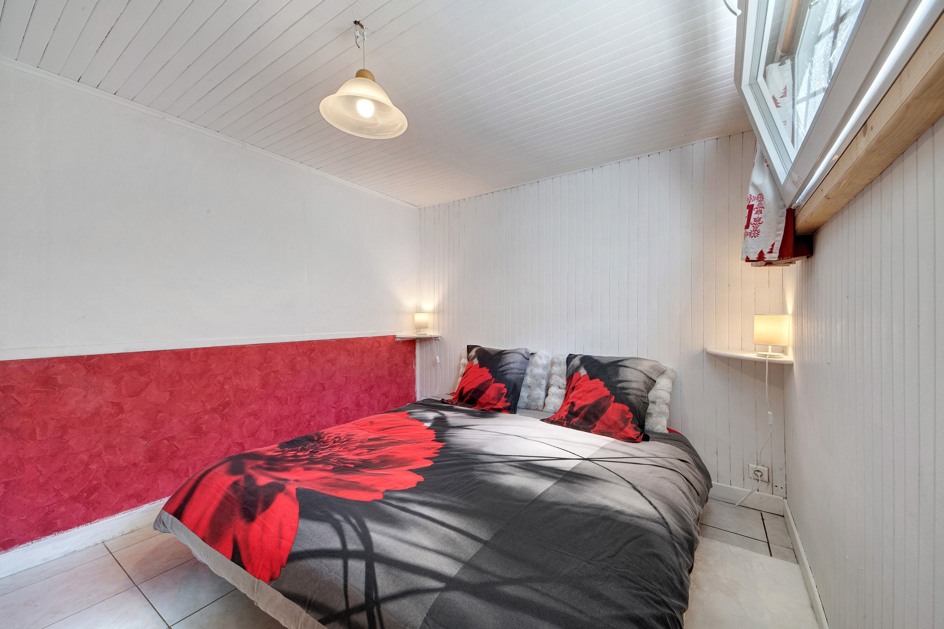 A bedroom with a bed, two bedside lamps, a ceiling light, and a window with blinds.