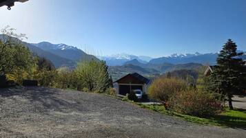 A gravel driveway leading to a wooden cabin with a garage, surrounded by greenery and mountains in the background.