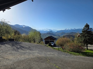 A gravel driveway leading to a wooden cabin with a garage, surrounded by greenery and mountains in the background. - Apartment 'Charmant Vue Mont-Blanc' with Mountain View and Wi-Fi (Onnion)