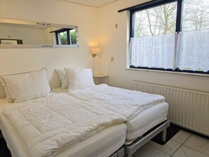 A double bed with white bedding, a bedside table, a wall-mounted mirror, and a window with a curtain. - Holiday Home With 2 Bedrooms (Oostkapelle)