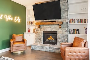 Una sala de estar con chimenea de piedra, sillones de cuero, una estantería y un letrero de neón.