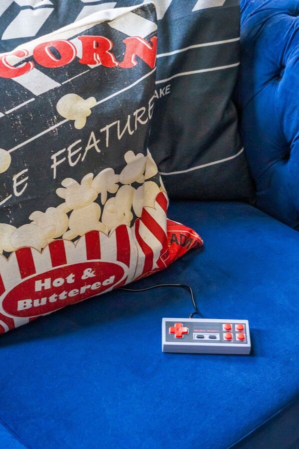 Un divano blu con un cuscino a tema pop corn e un controller per videogiochi d'epoca.