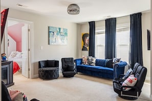 Ein Wohnzimmer mit einem blauen Sofa, schwarzen Sessel und einem gepolsterten Hocker, sowie einem Fernseher.