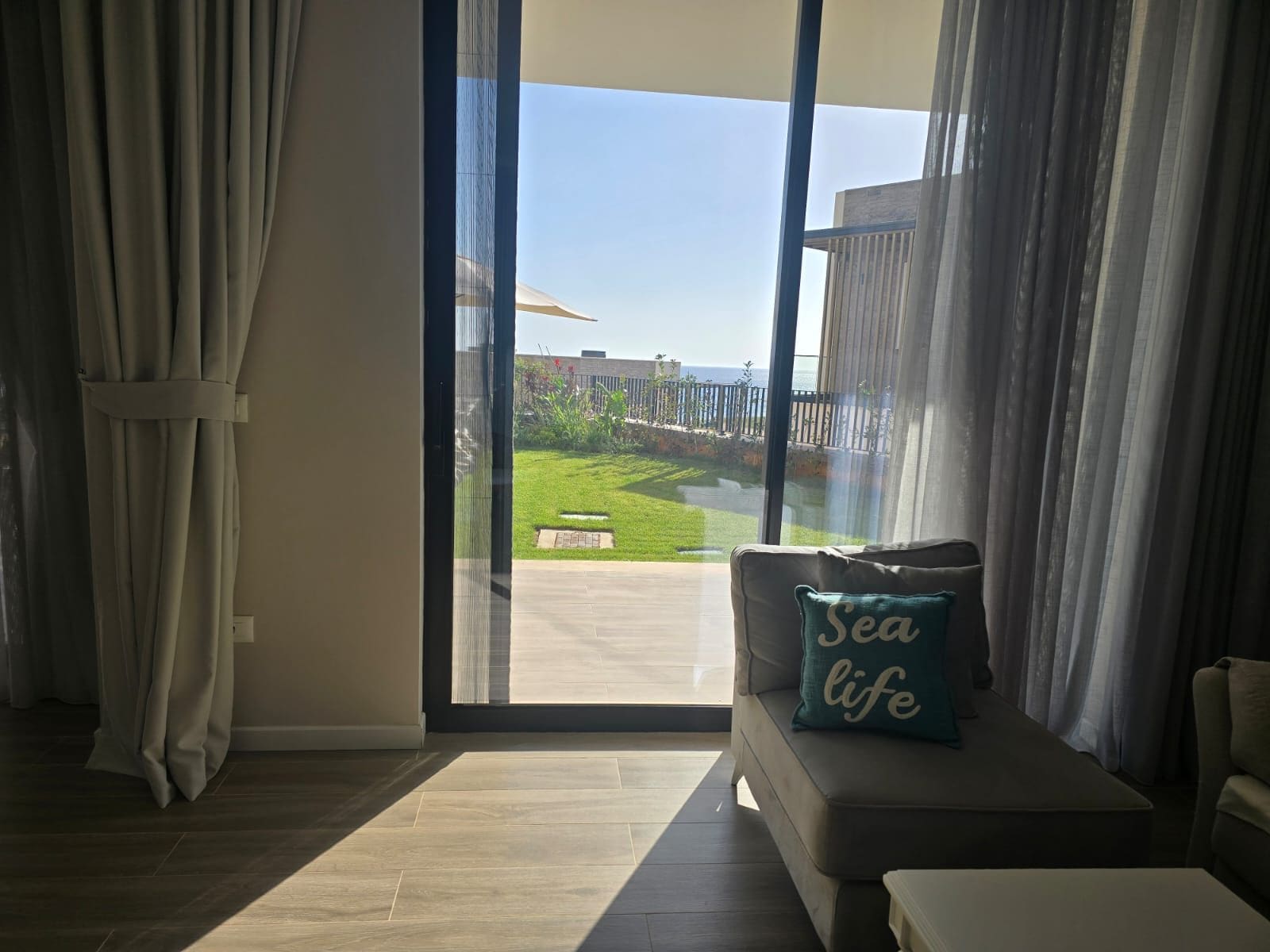 A room with a large sliding glass door leading to a patio with a view of the sea.