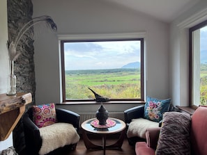 A room with a large window, two chairs, a small table, and a decorative lamp. - Mountainside Cottage, Dingle Wild Atlantic Way , Ireland (Dingle)