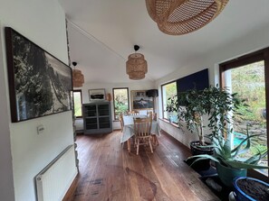 A spacious room with a wooden floor, a dining table with chairs, a large window with a view of greenery, and a radiator. - Mountainside Cottage, Dingle Wild Atlantic Way , Ireland (Dingle)