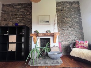A living room with a stone wall, a fireplace, a bookshelf, and a cozy chair. - Mountainside Cottage, Dingle Wild Atlantic Way , Ireland (Dingle)