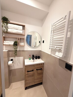 Ein modernes Badezimmer mit einem weißen Waschbecken, Holzschränken, einem Spiegel und einem Handtuchhalter.
